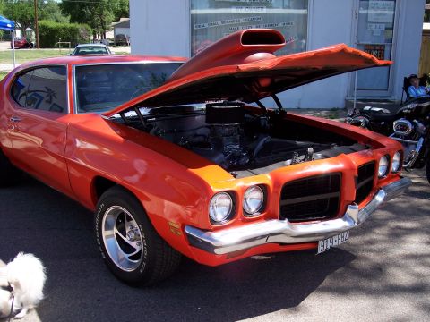 1972 Ford Ranchero - This orange muscle car, likely a 1970 model, is displayed with its hood open, revealing the engine and a prominent scoop.