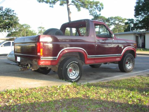 1981 Ford Bronco - Side view of a maroon Ford Bronco from the 1980s, its characteristic removable top and spare tire.