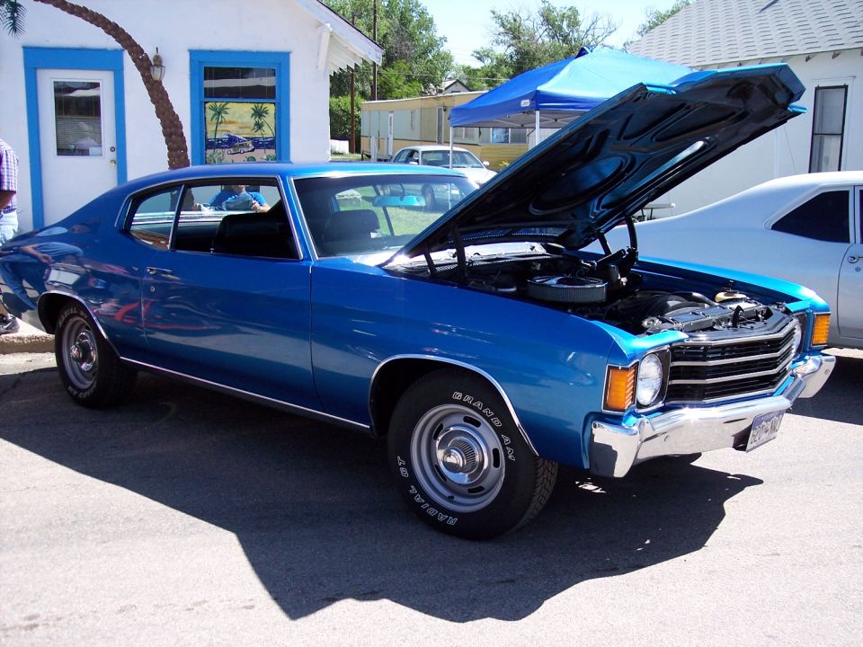 Blue coupe with hood open, showing engine. Chrome bumper and grille visible. Parked outdoors