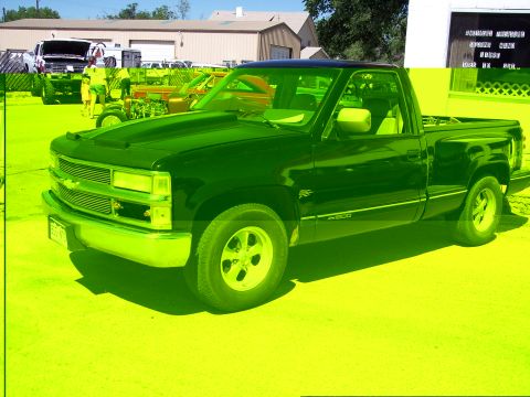 1972 Ford Ranchero - A black pickup truck is parked in a lot with other vehicles and buildings in the background.