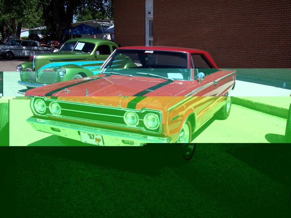 Front view of a red classic car with black and green stripes. A green classic car is behind it. License plate reads '67