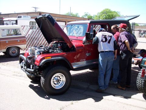1972 Ford Ranchero - A group of people examine the engine of a red Jeep with its hood raised at an outdoor car show.