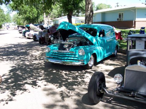 1972 Ford Ranchero - A teal panel van is displayed with its hood open at an outdoor car show, alongside other vehicles.