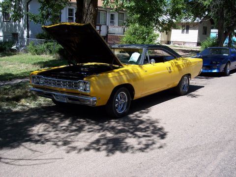 1972 Ford Ranchero - A yellow 1969 Plymouth Road Runner is parked on a street with its hood open, next to a blue car.