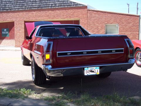 1972 Ford Ranchero - The rear of a red 1972 Ford Ranchero with racing stripes is visible, parked in front of a brick building.