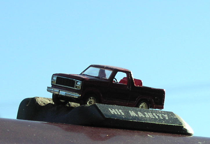 Diecast maroon Ford pickup on 'HIS MAJESTY' base posed against blue sky