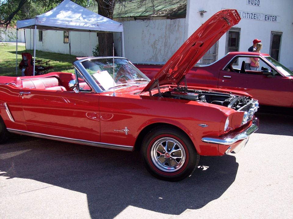 Red convertible with hood open, parked next to a red pickup truck