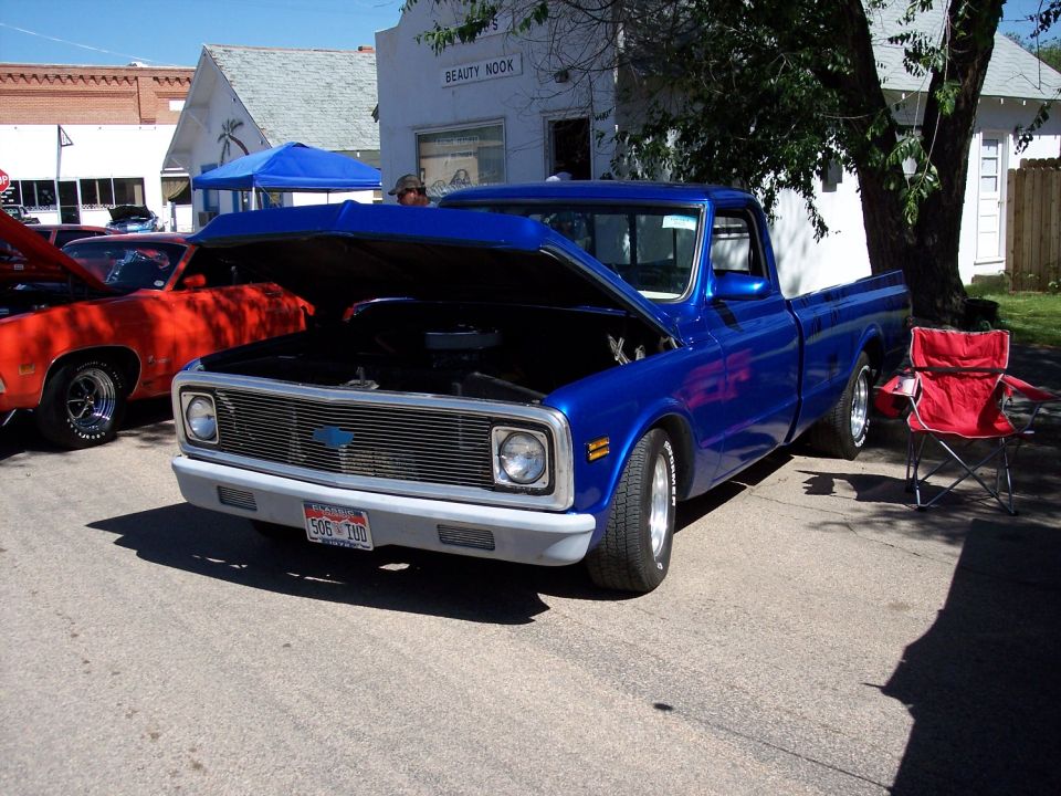 Blue pickup truck with hood open, parked next to a red car. A red chair is nearby