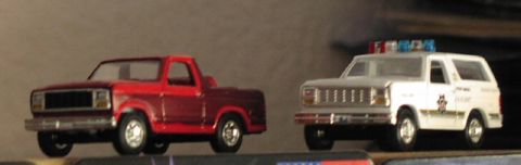 1981 Ford Bronco - Two toy trucks, a red pickup and a white police SUV, are displayed side-by-side.