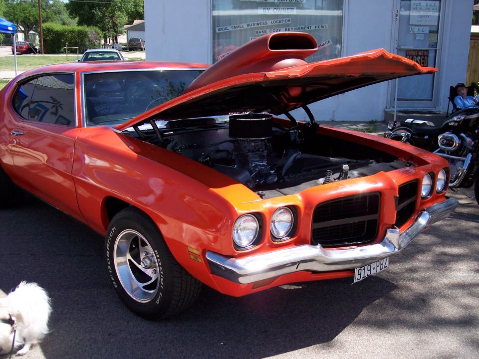 Orange muscle car with hood open, showing engine and scoop. License plate reads 919-PBZ