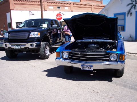 1972 Ford Ranchero - A blue 1972 Chevrolet Chevelle is displayed with its hood open, parked beside a black pickup truck at a car show.