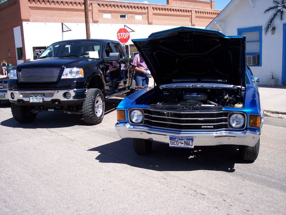 Blue 1972 Chevrolet Chevelle front view with hood open, parked next to a black pickup truck