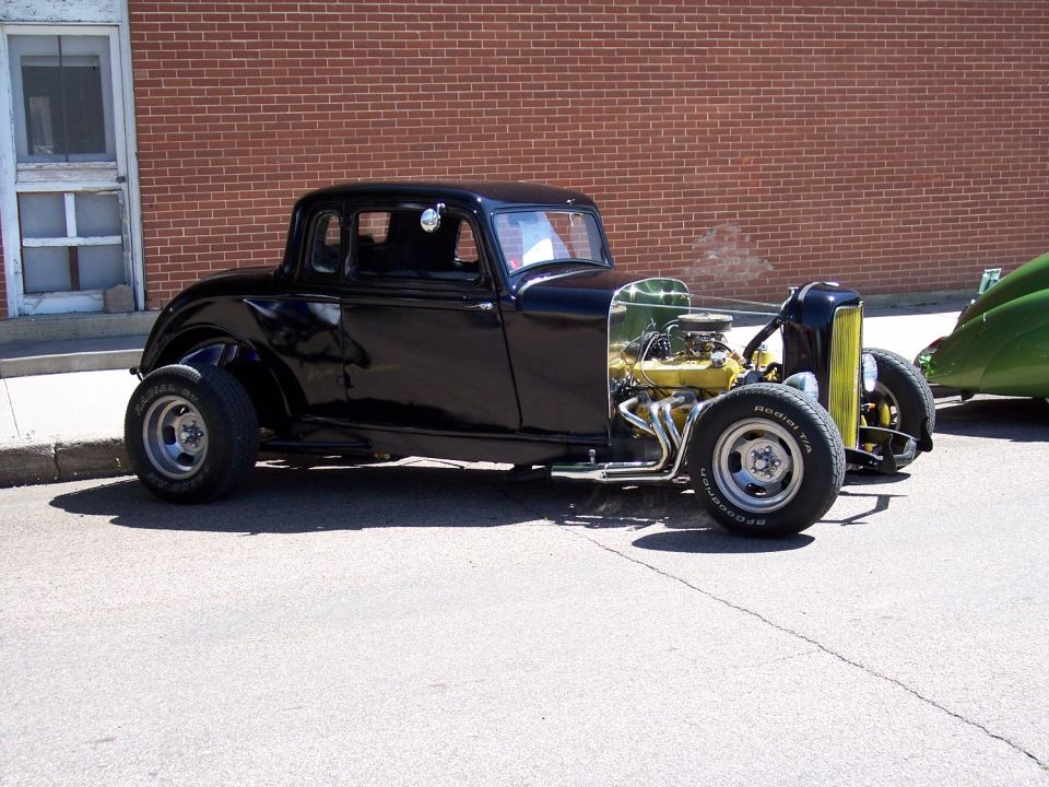 Black hot rod coupe with exposed engine and yellow accents on grille