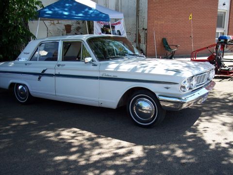 1972 Ford Ranchero - A white 1961 Ford Falcon sedan is parked outdoors under a blue tent, with brick building in the background.