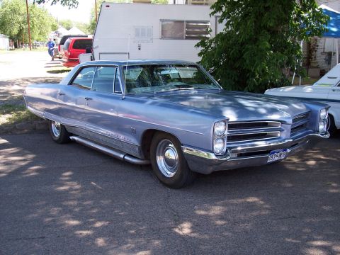1972 Ford Ranchero - A light blue 1965 Pontiac Bonneville is parked outdoors, showing its front and side profile.
