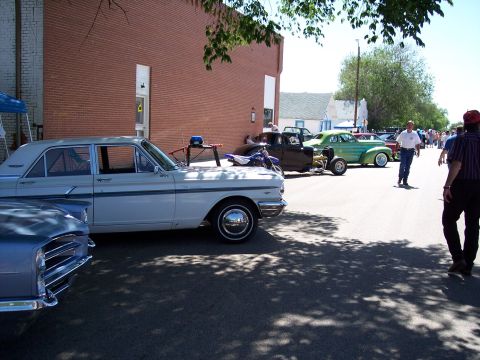1972 Ford Ranchero - A white sedan from the 1960s is parked on a street lined with other vehicles and buildings.