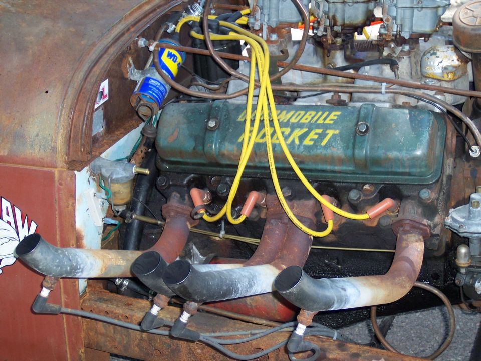Engine with green valve covers reading "Oldsmobile Rocket", custom exhaust pipes, and yellow spark plug wires