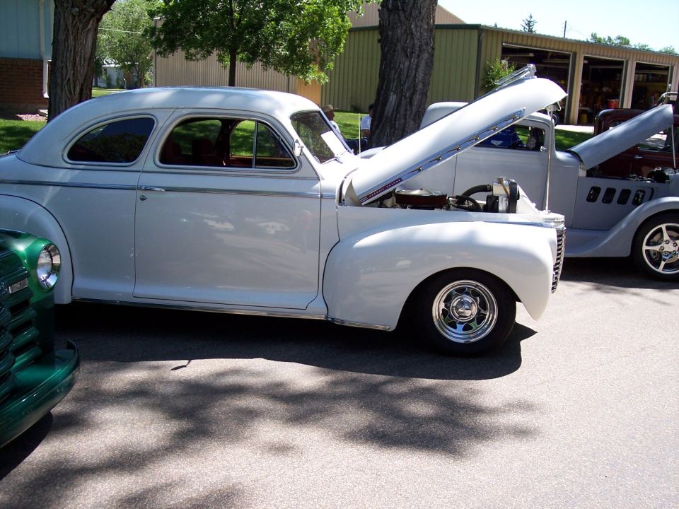 White coupe side view, hood open, chrome wheels
