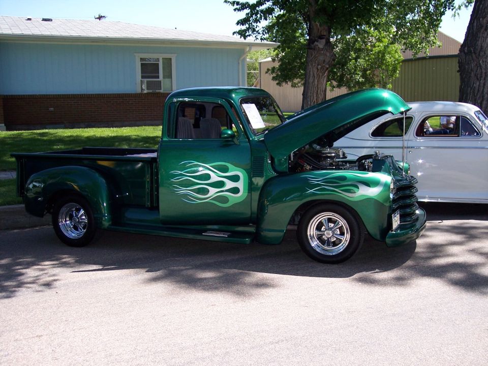 Green pickup truck with flame decals and hood open, parked next to a white car