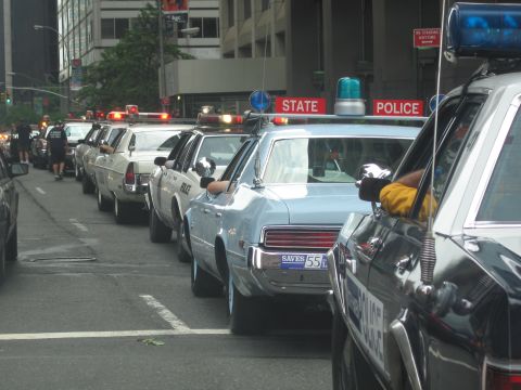1991 Ford LTD Crown Victoria - Vintage light blue State Police sedans with roof beacons line a downtown street under a red STATE POLICE banner.