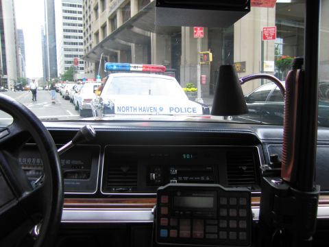 1991 Ford LTD Crown Victoria - Looking out a windshield over a wood-trimmed dash and two-way radio at a North Haven Police sedan parked ahead on a city street.