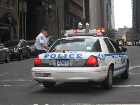 1991 Ford LTD Crown Victoria - police officer stands beside a white NYPD Highway Patrol Ford Crown Victoria with car number 2867 on a downtown street.