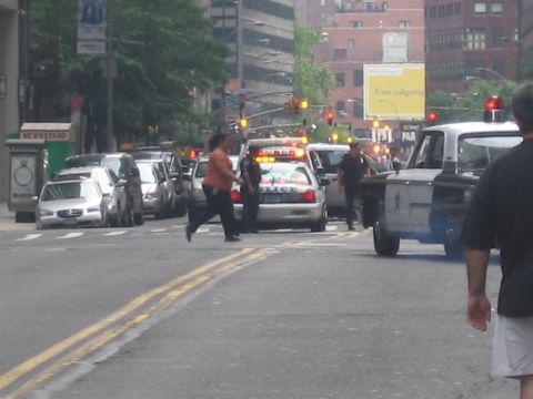 1991 Ford LTD Crown Victoria - police car with emergency lights flashing stops at a city intersection while a man crosses the street and a pickup pulls alongside.
