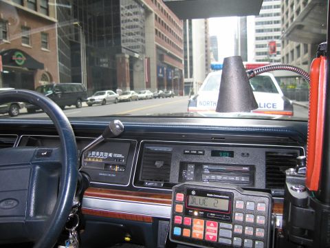 1991 Ford LTD Crown Victoria - Ford steering wheel, wood-trimmed dash and two-way police radio frame a view of a North Haven Police sedan ahead on a city street.