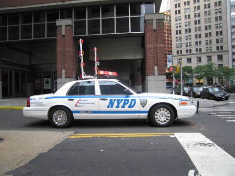 1991 Ford LTD Crown Victoria - white and blue NYPD Auxiliary Ford Crown Victoria with roof lightbar is parked broadside on a downtown street by a brick building.