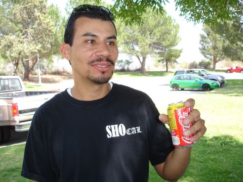 1993 Ford Taurus - A man holds a Coca-Cola can with cars parked in a grassy area behind him.