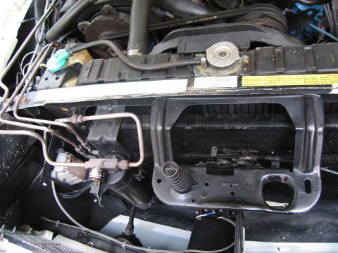1991 Ford LTD Crown Victoria - Close-up of an engine bay showing the radiator core support, cooling lines and a yellow antifreeze warning decal.