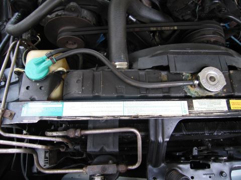 1991 Ford LTD Crown Victoria - Close-up of an engine compartment with radiator, upper hose, alternator and a green reservoir cap above warning decals.