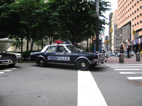 1991 Ford LTD Crown Victoria - dark blue and white North Haven Police sedan parked at a downtown crosswalk near other cars and trees.