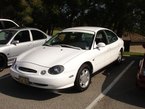 1993 Ford Taurus - A white sedan is parked in a lot next to another vehicle.