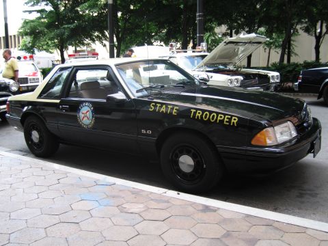1991 Ford LTD Crown Victoria - black Florida State Trooper Ford Mustang 5.0 coupe with gold lettering parked at an outdoor car show.