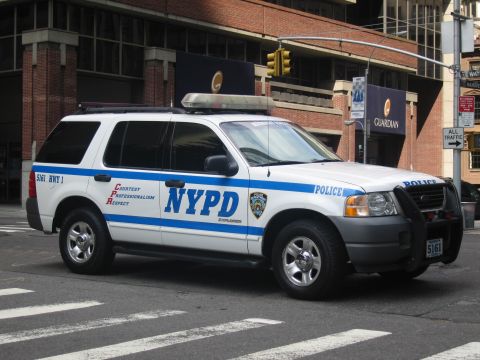 1991 Ford LTD Crown Victoria - white and blue NYPD Ford Explorer highway-patrol SUV parked at a city crosswalk by a brick building.