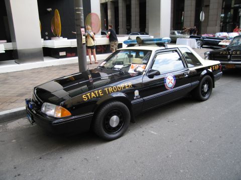 1991 Ford LTD Crown Victoria - black Florida Highway Patrol State Trooper Mustang coupe with gold lettering parked along a downtown curb.