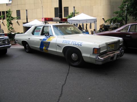 1991 Ford LTD Crown Victoria - white vintage State Police sedan with blue-and-yellow door stripe and roof light parked at an outdoor show.