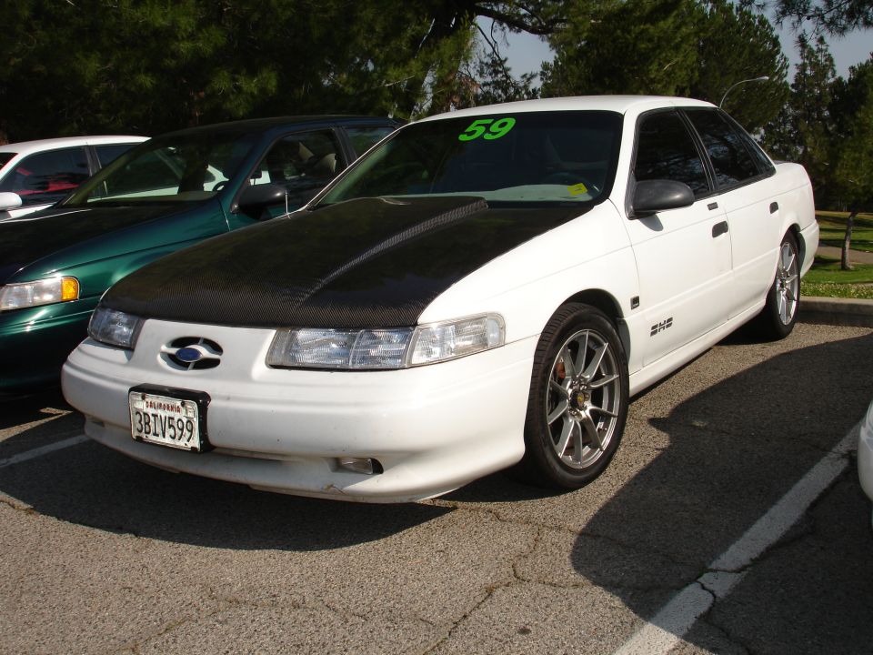 White 1993 Ford Taurus with a black aftermarket hood, parked next to a green car