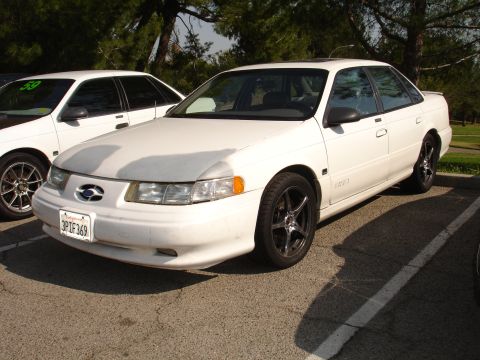 1993 Ford Taurus - A white 1993 Ford Taurus sedan is parked in a lot, with another white car visible to its left.