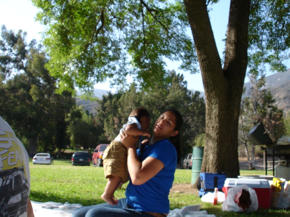 Woman holding a baby at a park picnic with cars in the background