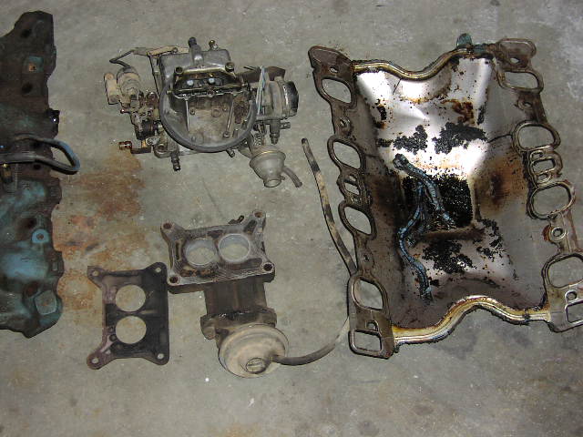 Disassembled intake manifold, carburetor, spacer and EGR parts laid out on concrete