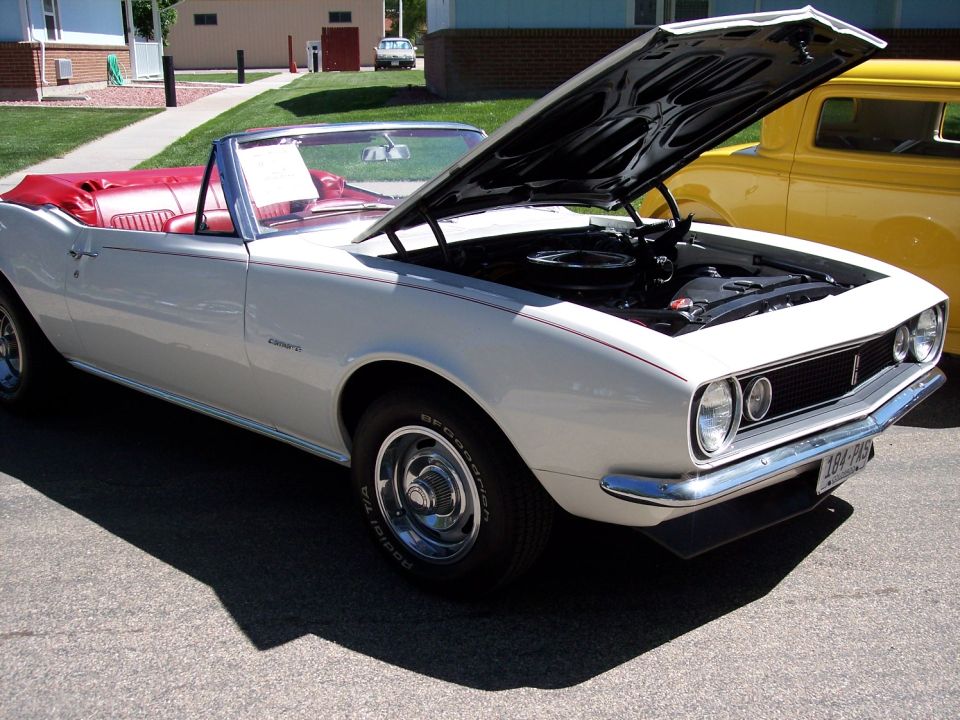 White 1967 Chevrolet Camaro convertible with red interior, hood open. Yellow car behind it