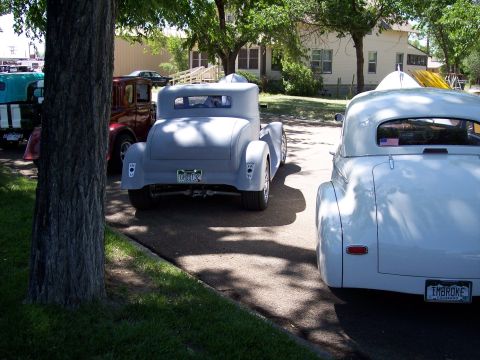 1972 Ford Ranchero - Two classic cars, a gray coupe and a white convertible, are parked on a street under dappled sunlight.