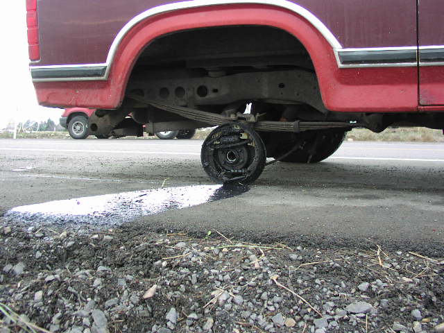 Underside rear of red truck showing leaf spring and brake drum dripping over wet pavement