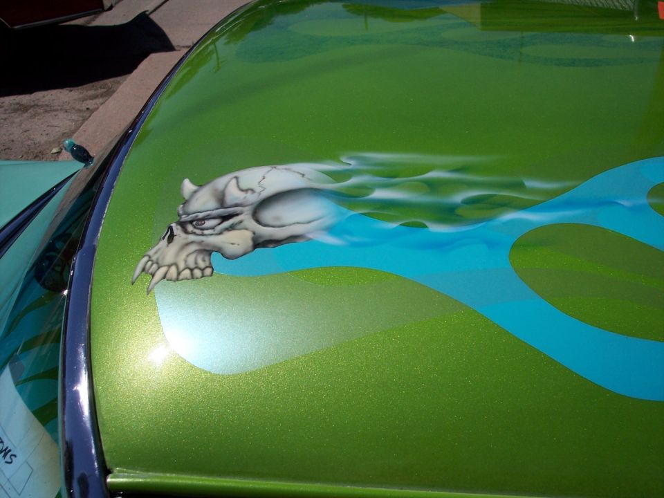 Green car hood with airbrushed skull and blue flames. Some text is visible on a paper below the windshield