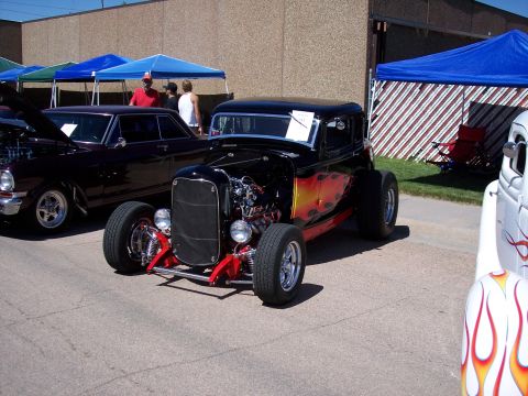 1972 Ford Ranchero - A black hot rod with flame graphics and an exposed engine is parked at a car show.