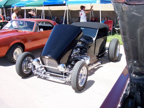 1972 Ford Ranchero - A black hot rod is displayed with its hood open, revealing the engine, next to another classic car at a show.