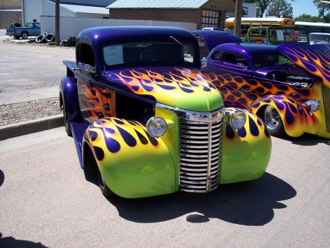 1972 Ford Ranchero - A custom hot rod truck with a vibrant flame paint job is displayed at an outdoor car show.