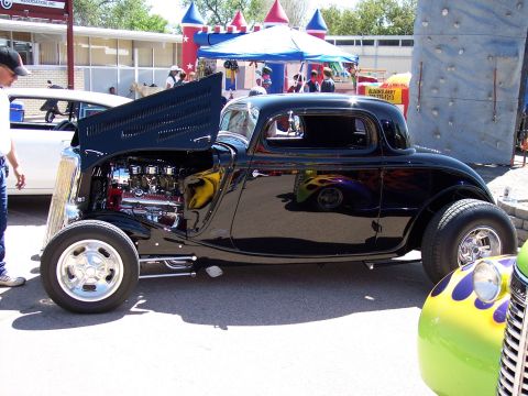 1972 Ford Ranchero - A black hot rod coupe is displayed at an outdoor event with its hood open, revealing a chrome engine.